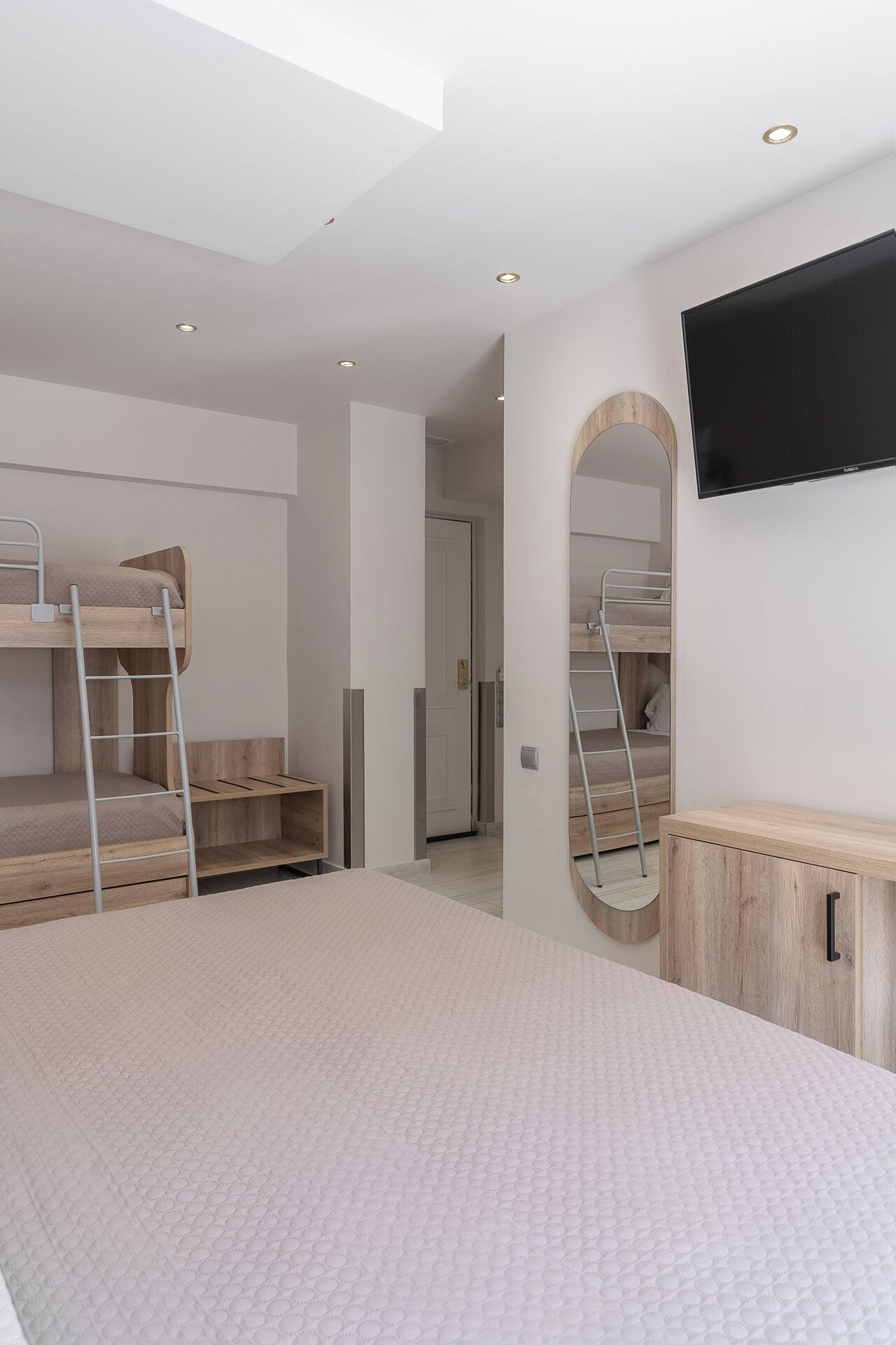 A modern bedroom with bunk beds, a TV, and a mirror.