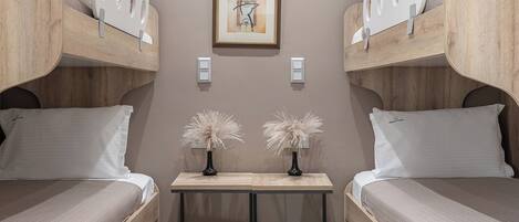 A room with two bunk beds, a small table with two vases, and two framed artworks on the wall.