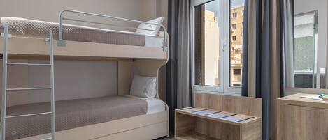 A compact hotel room with a bunk bed, a desk, and a window with a city view.