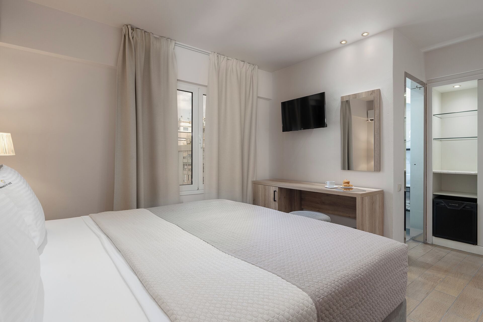 Una habitación de hotel con cama, escritorio, televisor, espejo y armario.