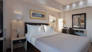 Habitación de hotel con una cama grande, una mesita de noche, un escritorio, una silla, un espejo y un cuadro en la pared.