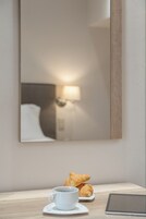 Una habitación de hotel con una mesita de noche que presenta una taza de café, un croissant y una tableta.