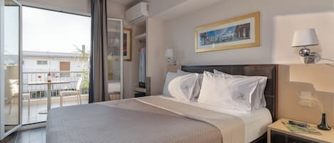 A hotel room with a bed, a nightstand, a lamp, a painting, and a view of the outside.