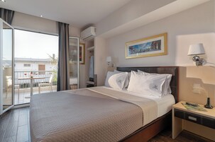 A hotel room with a bed, a nightstand, a lamp, a painting, and a view of the outside.