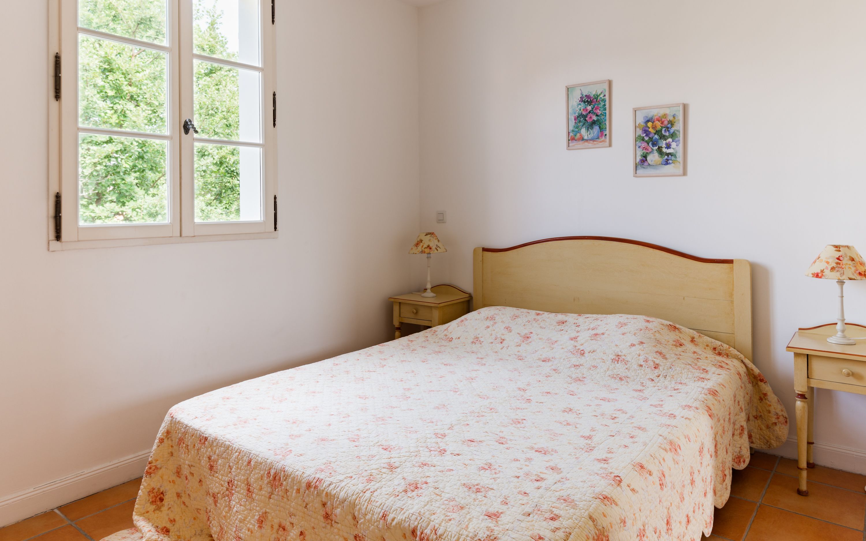 Un dormitorio con una cama, una mesita de noche, una lámpara y dos cuadros en la pared.