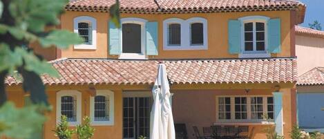 A two-story house with a tiled roof, a swimming pool, and outdoor furniture.