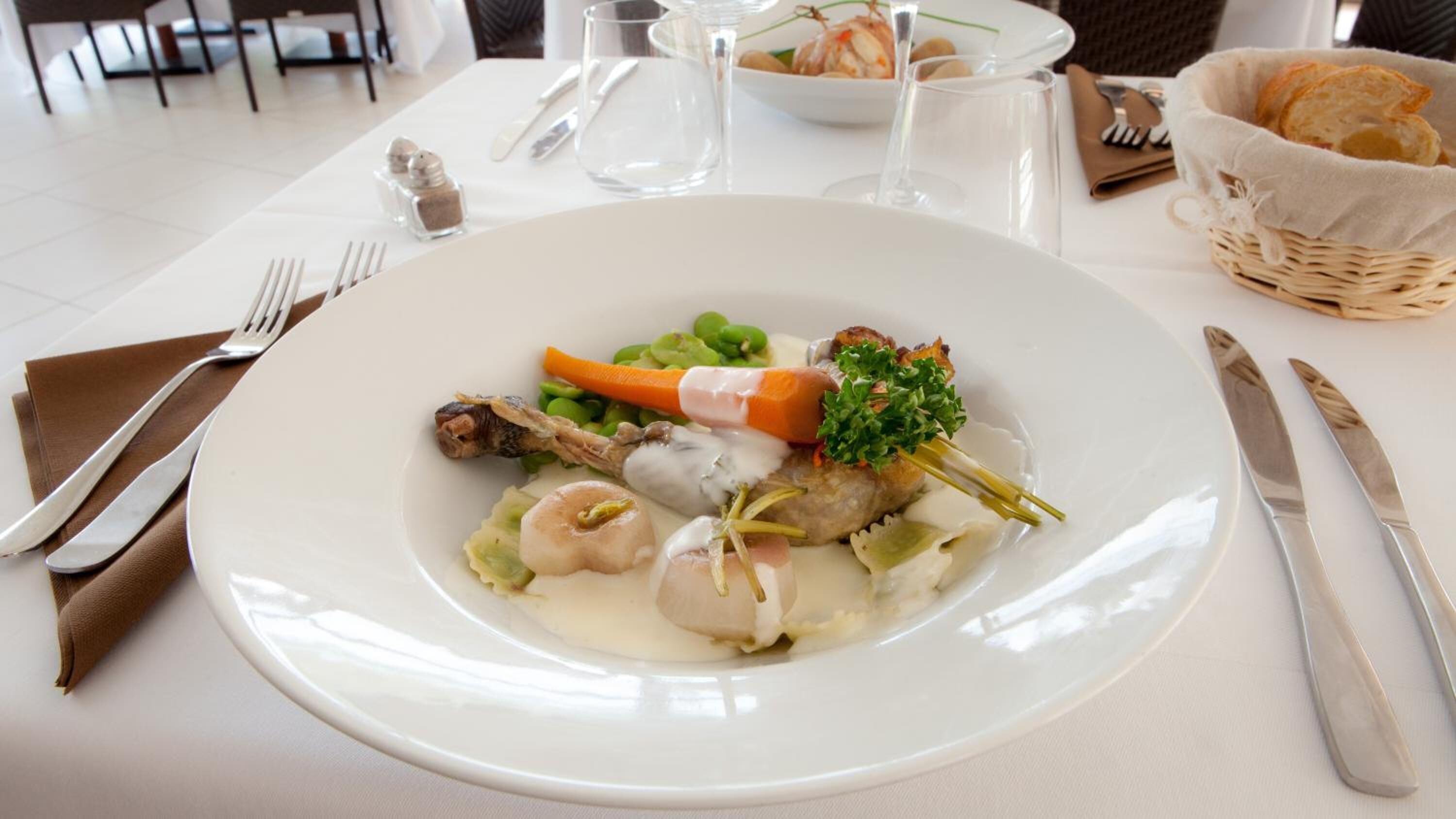A white plate with a seafood dish, including shrimp, carrots, and greens, on a white tablecloth.