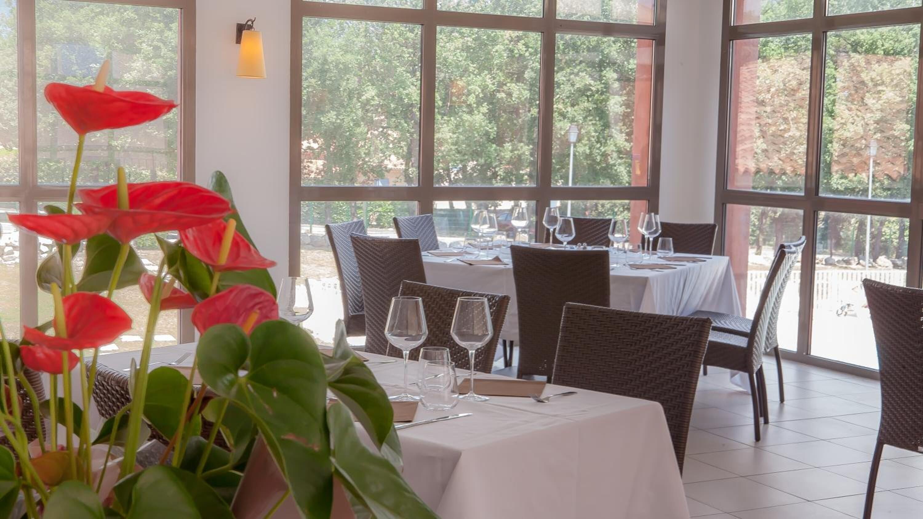 Un restaurant doté de grandes fenêtres, de chaises en osier et de tables dressées pour le service.