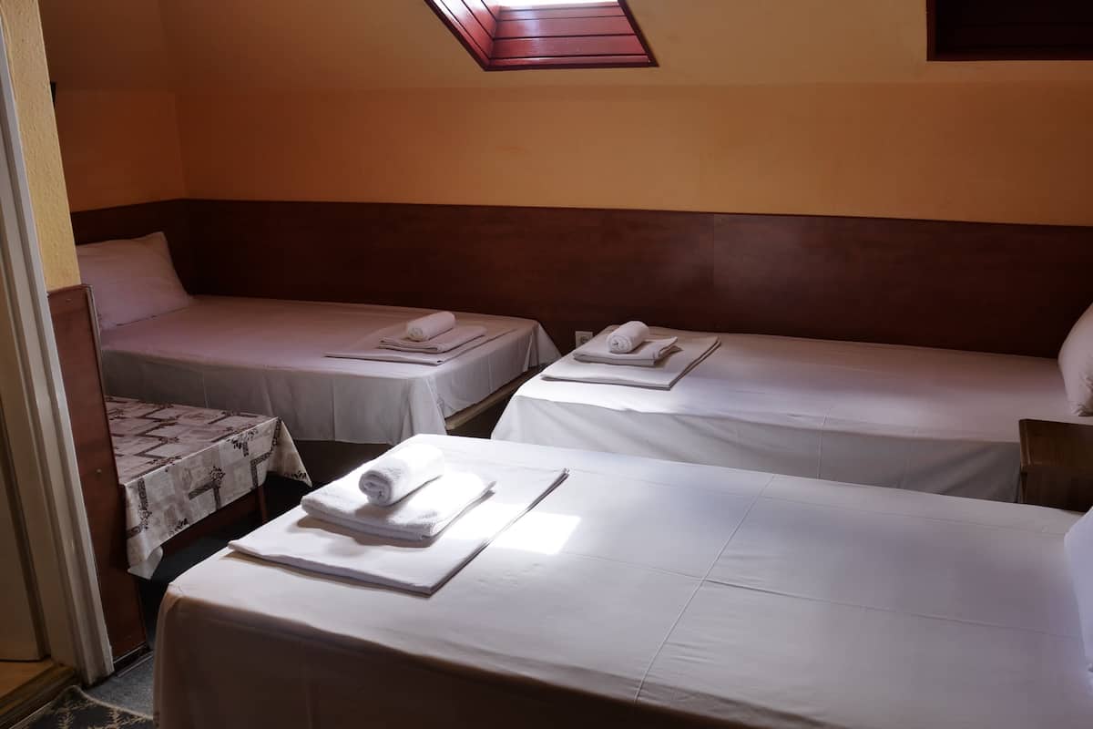 Ein Zimmer mit zwei Einzelbetten, jeweils ausgestattet mit einem zusammengerollten Handtuch und Kissen, sowie einer Schlafcouch mit Kissen.