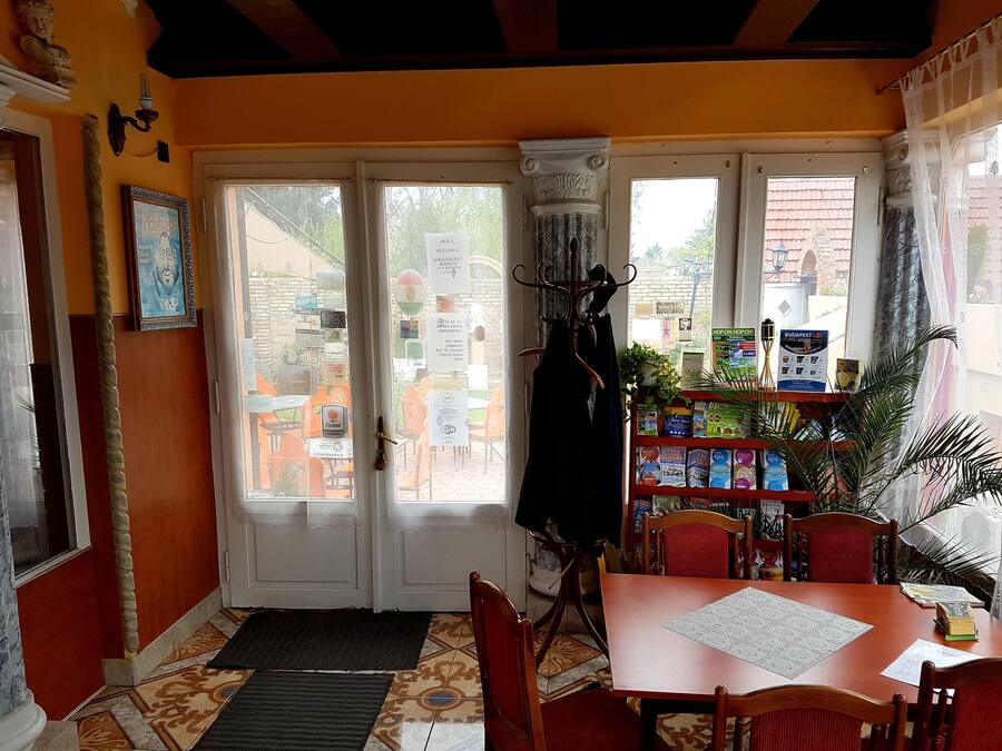 A room with a wooden table and chairs, a bookshelf with various items, and a view of the outside through large windows.