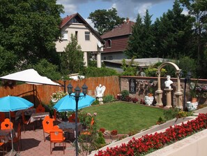 An outdoor patio with tables and chairs, a brick pathway, and a garden with flowers and a statue. - ATTILA HOTEL BUDAPEST (Budapest)