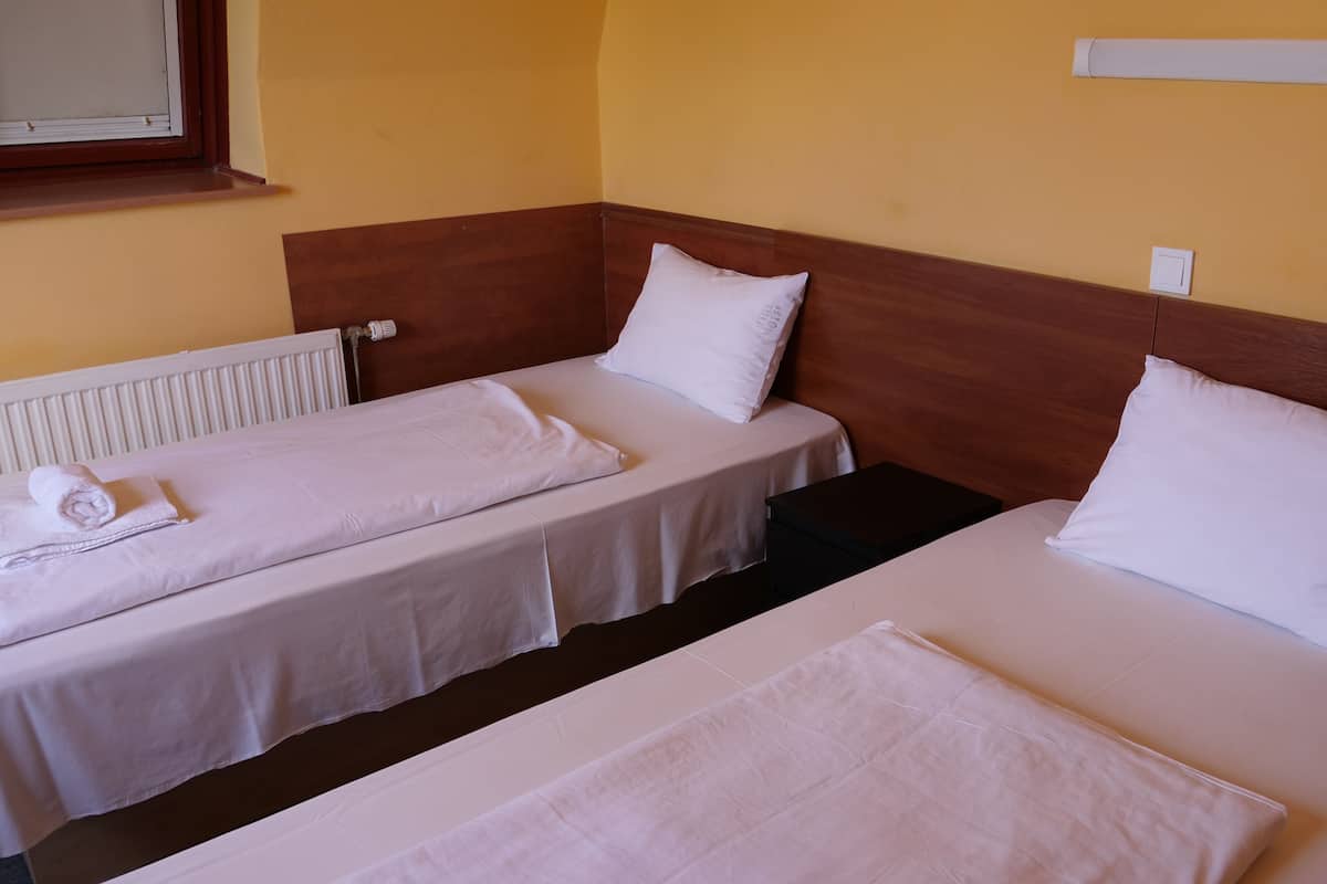 Ein Hotelzimmer mit zwei Einzelbetten, weißen Leinentüchern, einem hölzernen Kopfteil, einem Heizkörper und einem Fenster mit Jalousien.