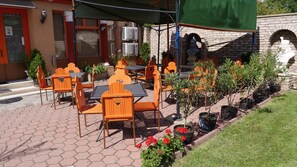 An outdoor seating area with orange chairs and tables, a brick wall with a statue, and air conditioning units on the building. - ATTILA HOTEL BUDAPEST (Budapest)