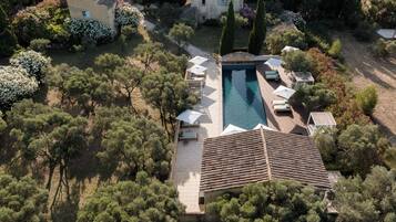 An aerial view of a property with a swimming pool surrounded by lounge chairs, a patio area, and dense greenery.