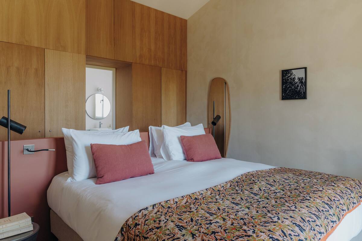 Habitación de hotel con una cama grande, paneles de madera en las paredes, un espejo redondo y un cuadro enmarcado.