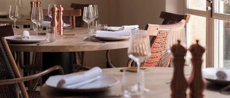 Une table à manger dressée avec des assiettes, des couverts et des verres à vin, ainsi que des salières et des poivrières posées sur la table.
