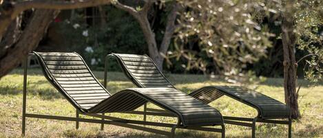 Two outdoor lounge chairs with metal frames and cushioned seats, positioned on a grassy area with trees in the background.