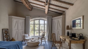 Una habitación acogedora con cama, escritorio y silla. Hay un ventanal con cortinas y un cuadro en la pared.