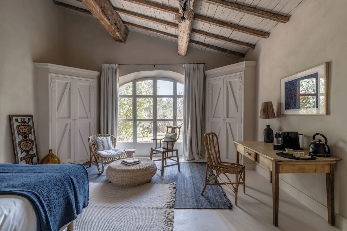 Una habitación acogedora con cama, escritorio y silla. Hay un ventanal con cortinas y un cuadro en la pared.