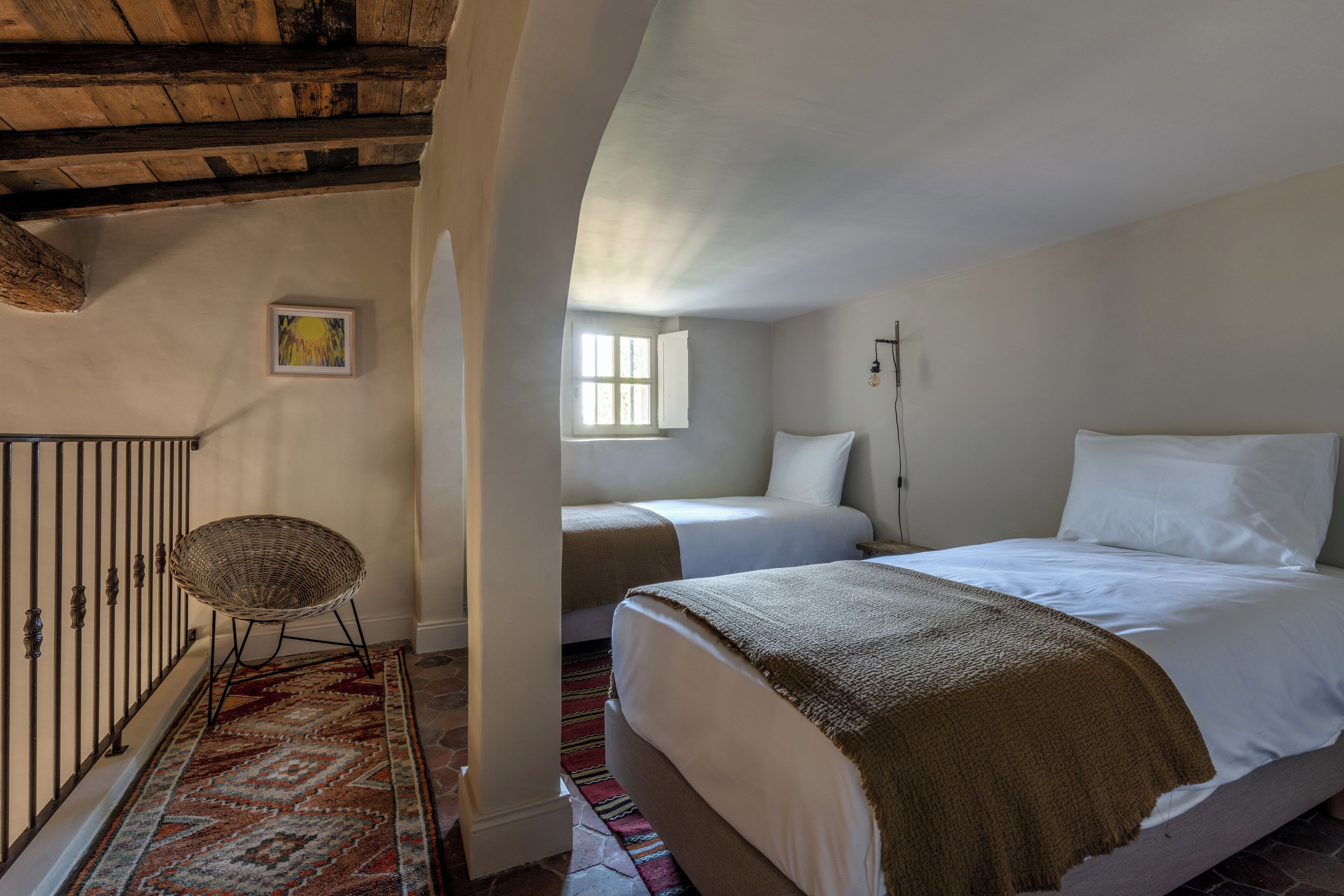 A bedroom with a large bed, a smaller bed, a chair, a window, and a picture on the wall.