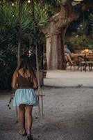 Uma pessoa caminhando por um caminho de areia, com um balanço pendurado em uma árvore, cercada por vegetação.