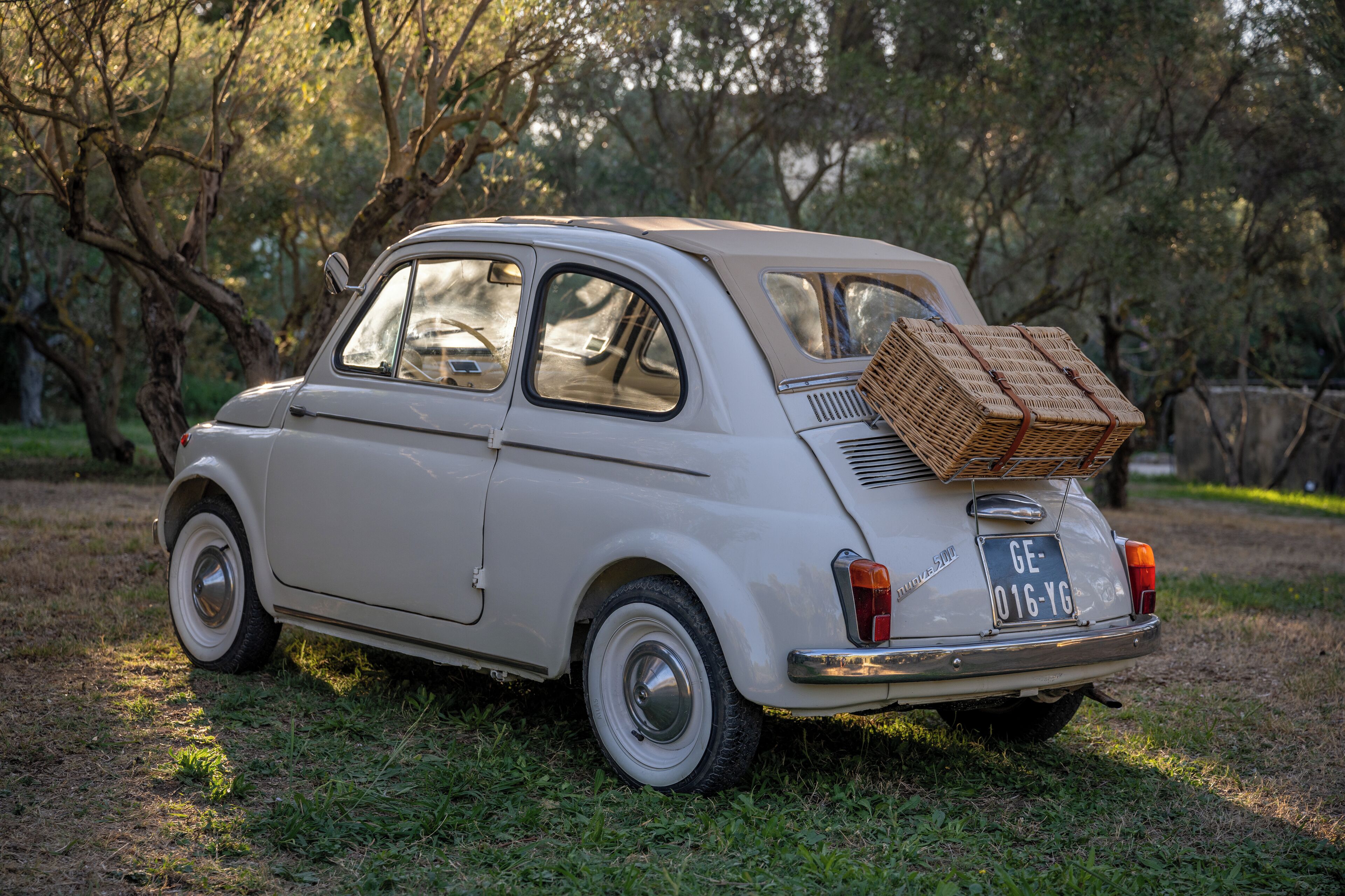 A vintage car parked in a grassy area with trees in the background.
