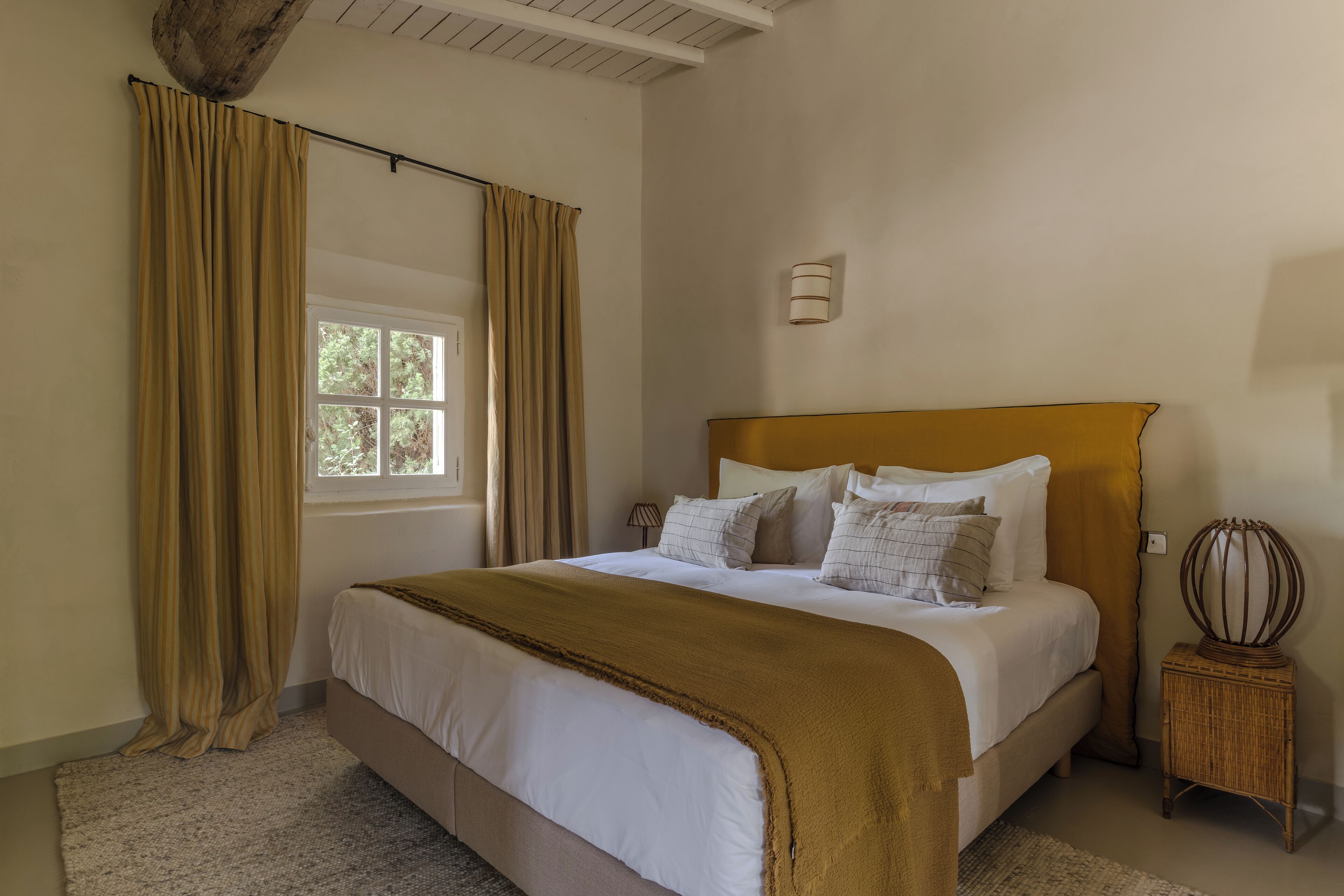 A bedroom with a large bed, a window, a bedside lamp, and a small table.