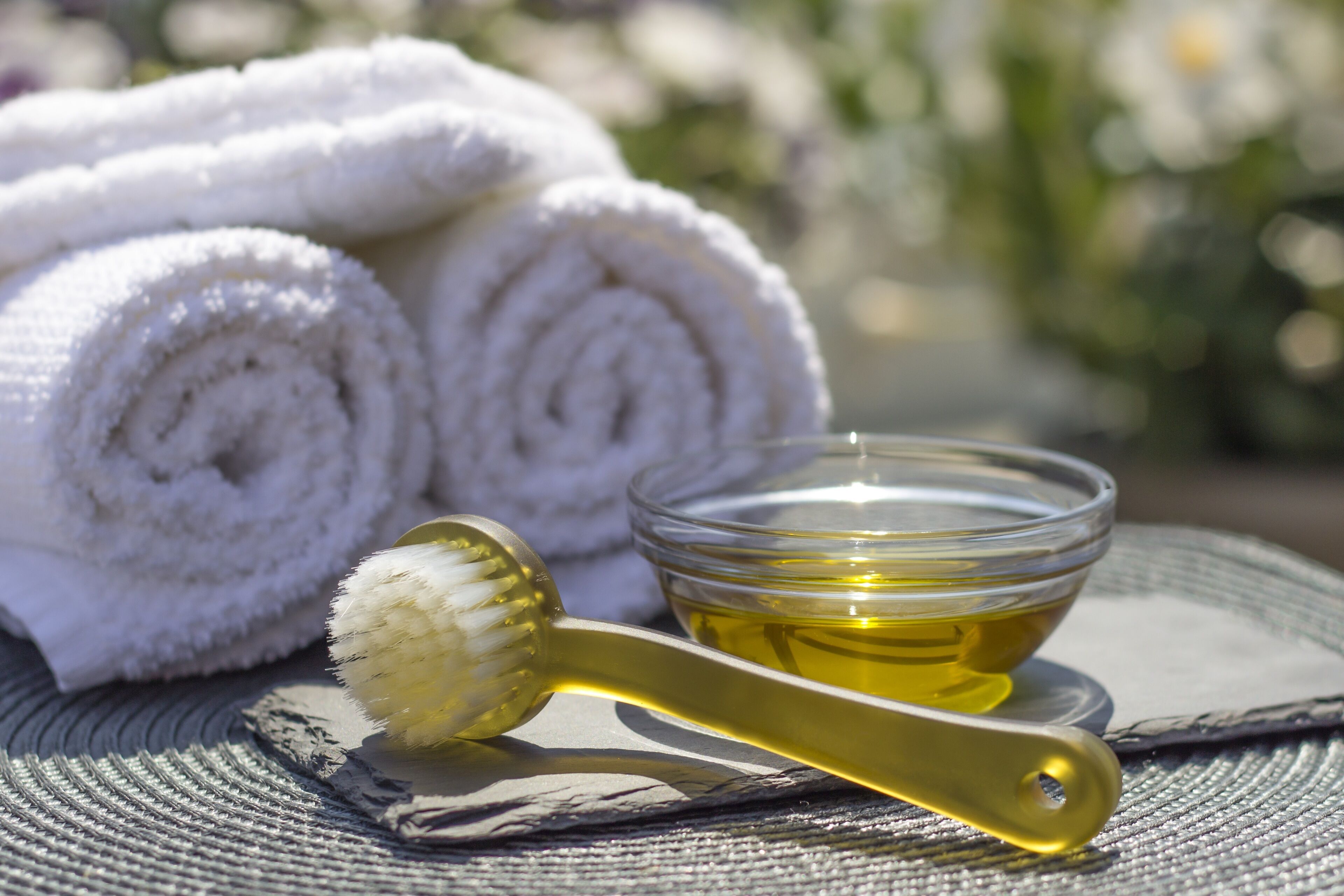 A rolled white towel, a yellow brush, and a glass bowl with a yellow liquid on a textured surface.