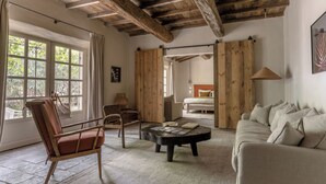 Una habitación con techo de madera, un ventanal con cortinas, una mesa de centro redonda, un sofá y una silla.