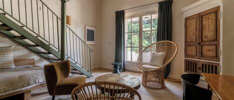 Una habitación acogedora con una escalera, sillas de mimbre, una mesa de madera y una cama.
