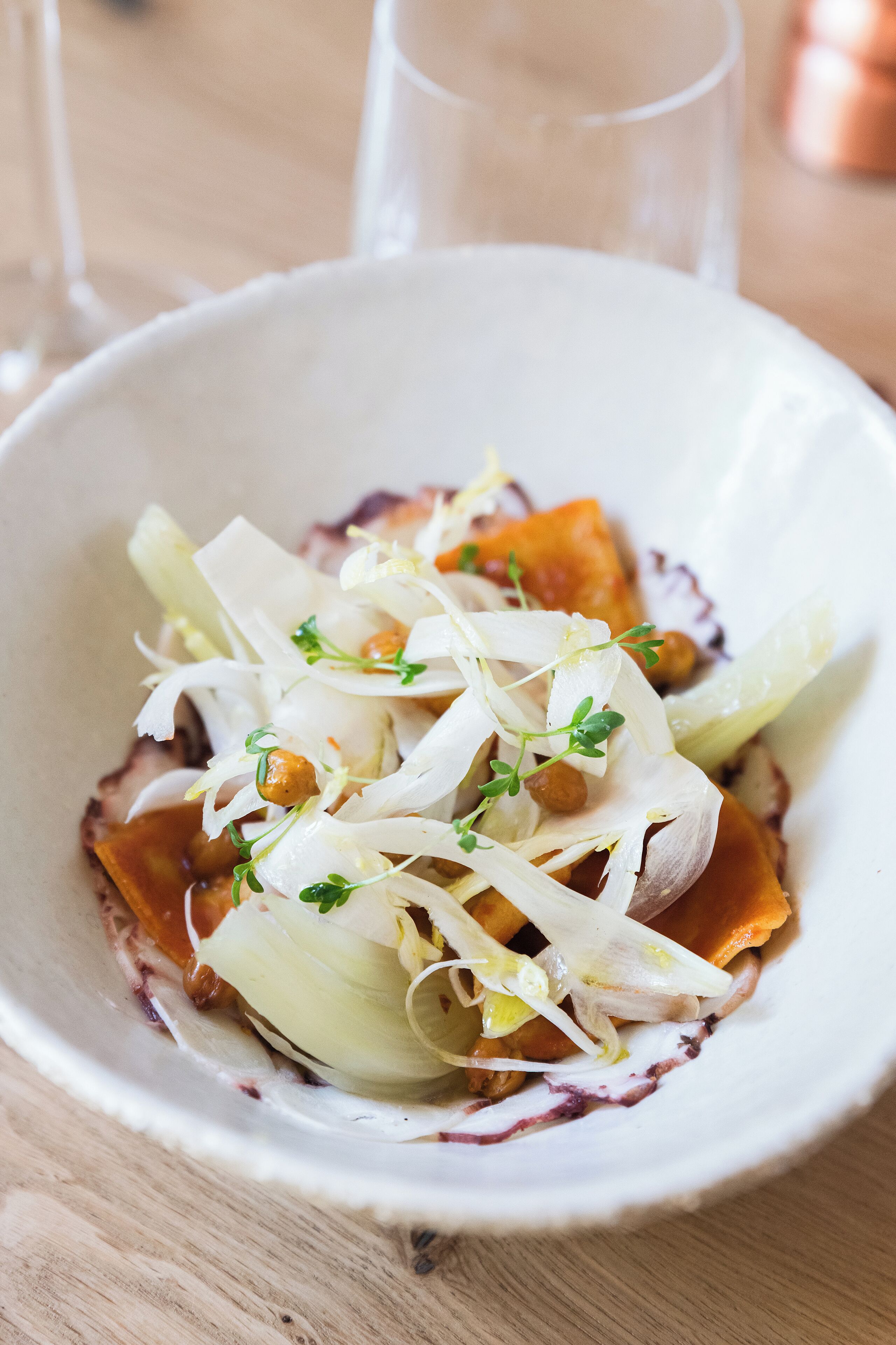 A white bowl containing a dish with vegetables and herbs.