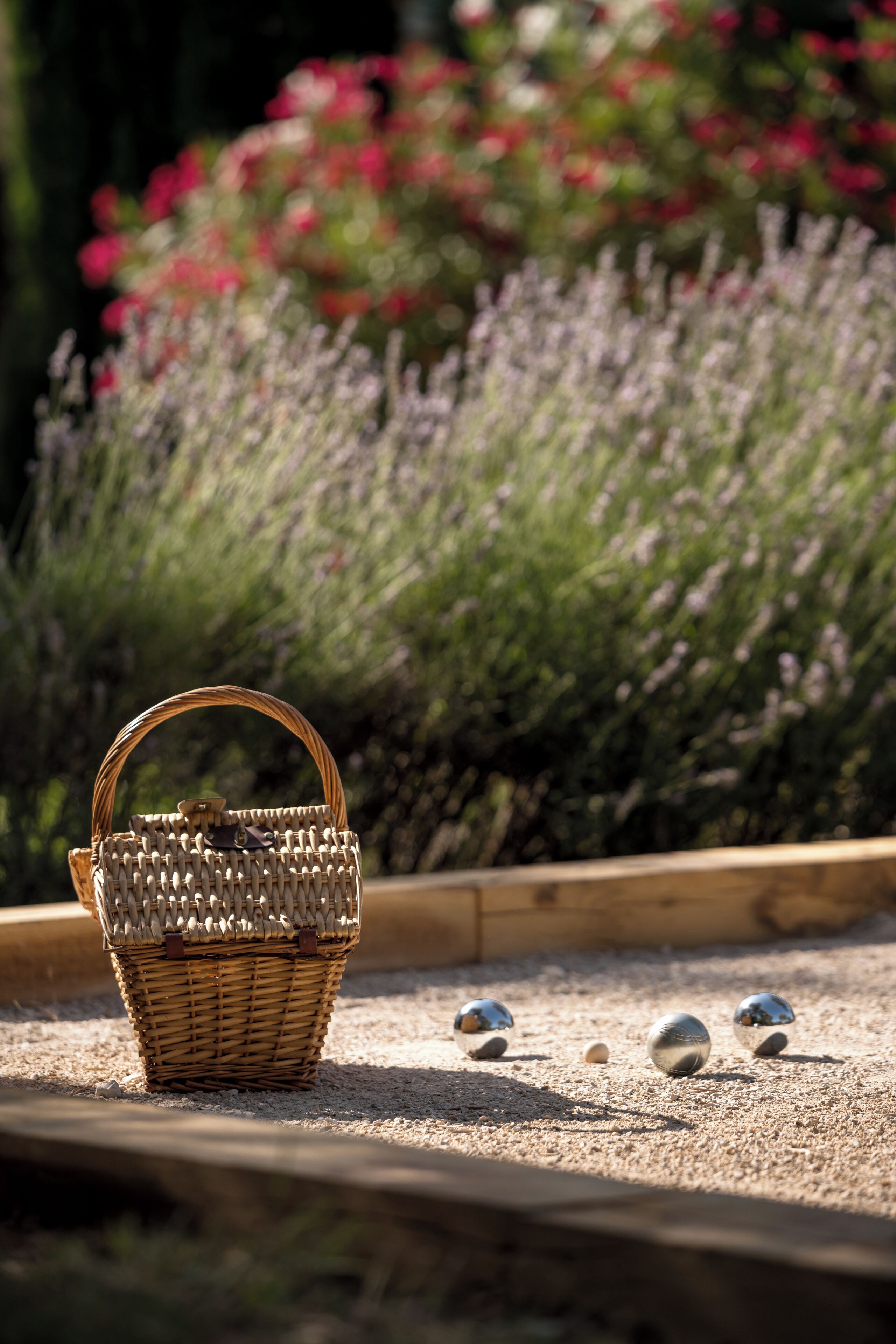 Un panier en osier doté d’une anse, posé sur un sol de gravier, entouré de plants de lavande et bordé de bois.