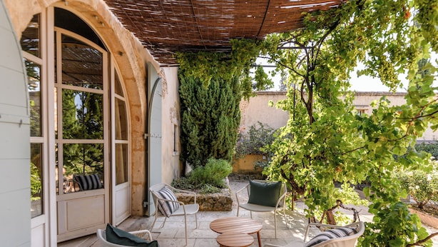 Un patio cubierto con mobiliario exterior, un muro de piedra y follaje.