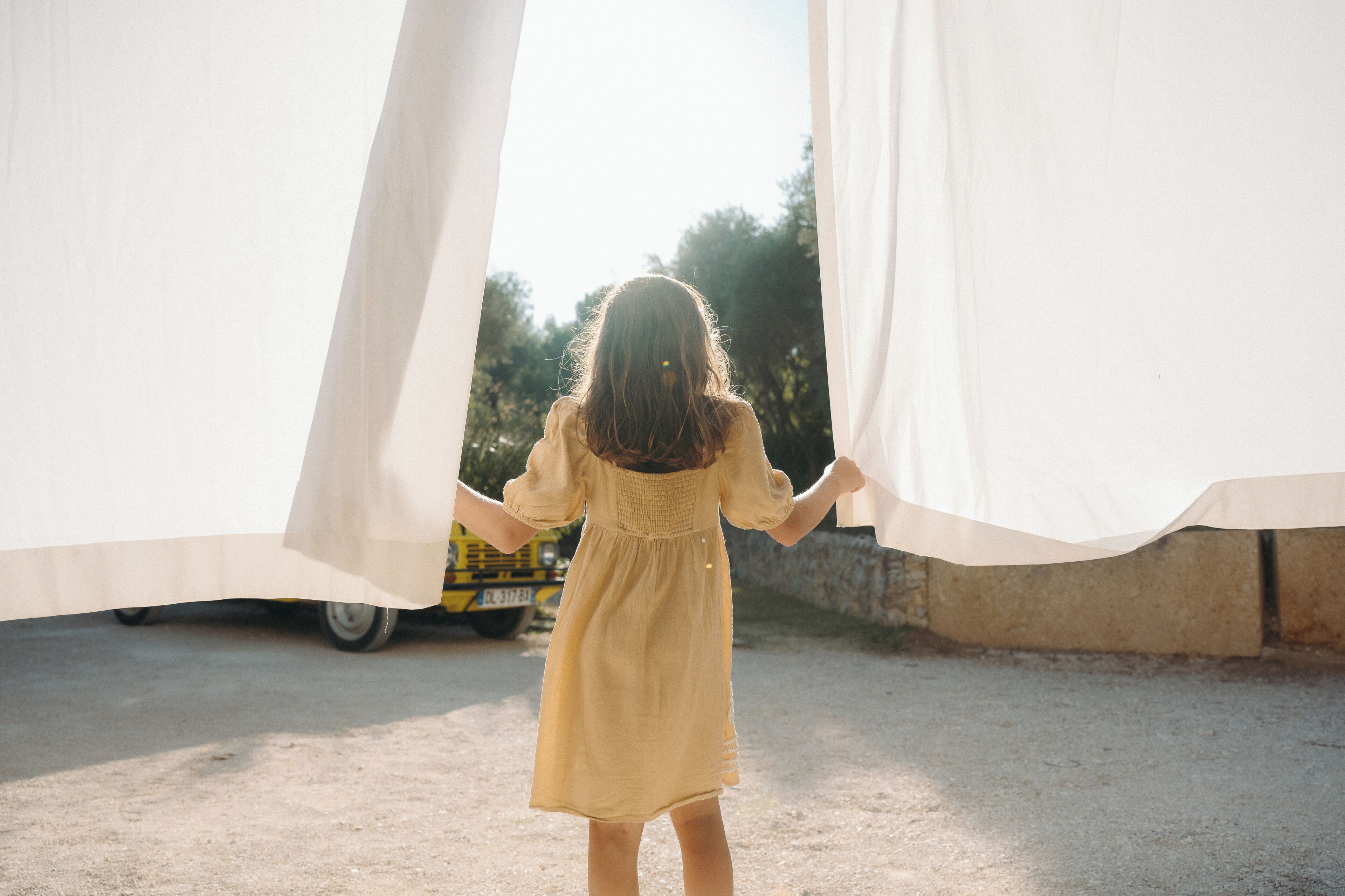 A child holding a white fabric, standing in an outdoor setting with a vehicle in the background.