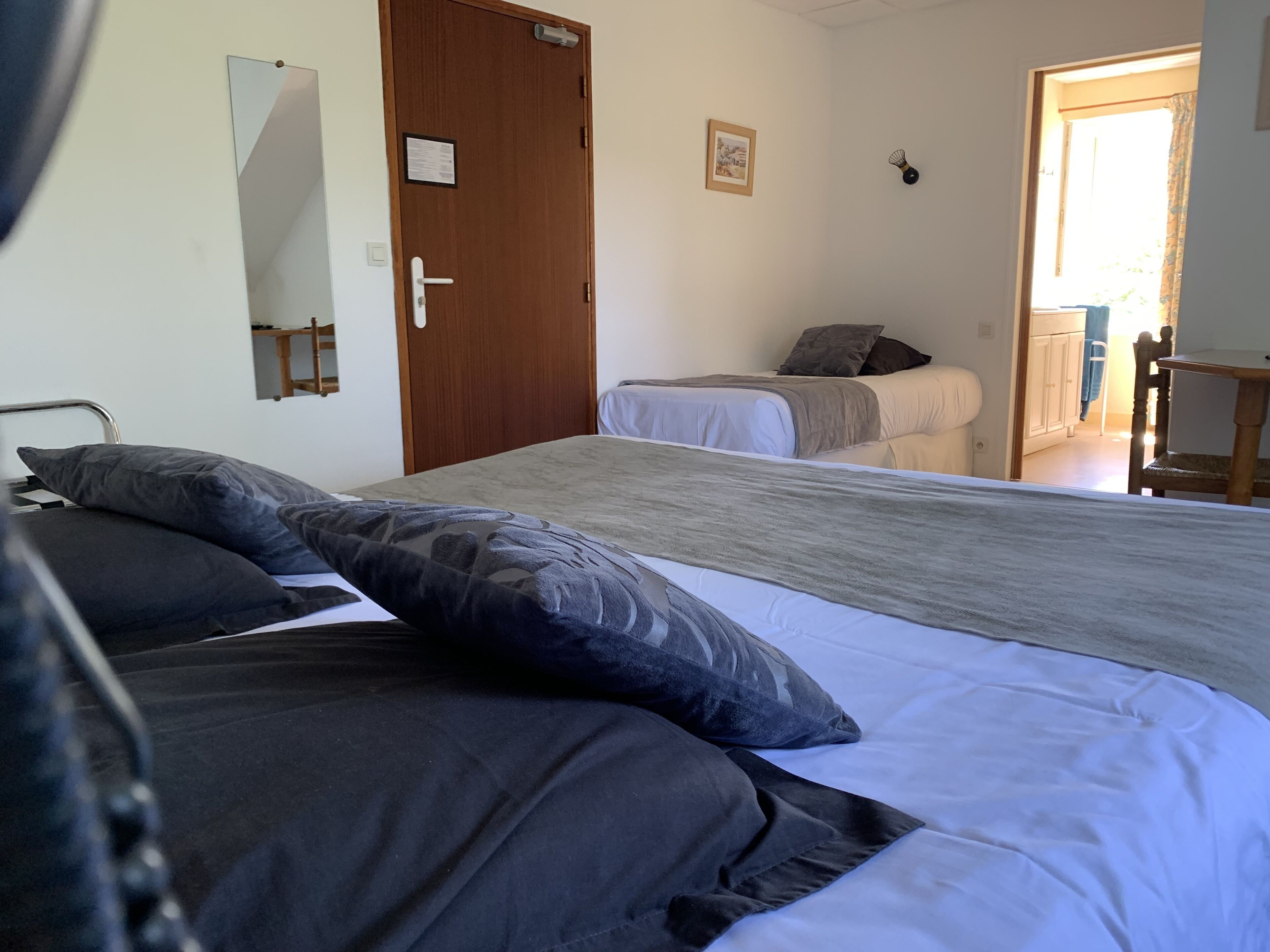 Une chambre avec deux lits, une porte en bois, un miroir et une petite table.