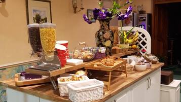 A buffet setup with various food items, a coffee dispenser, and a vase with flowers.