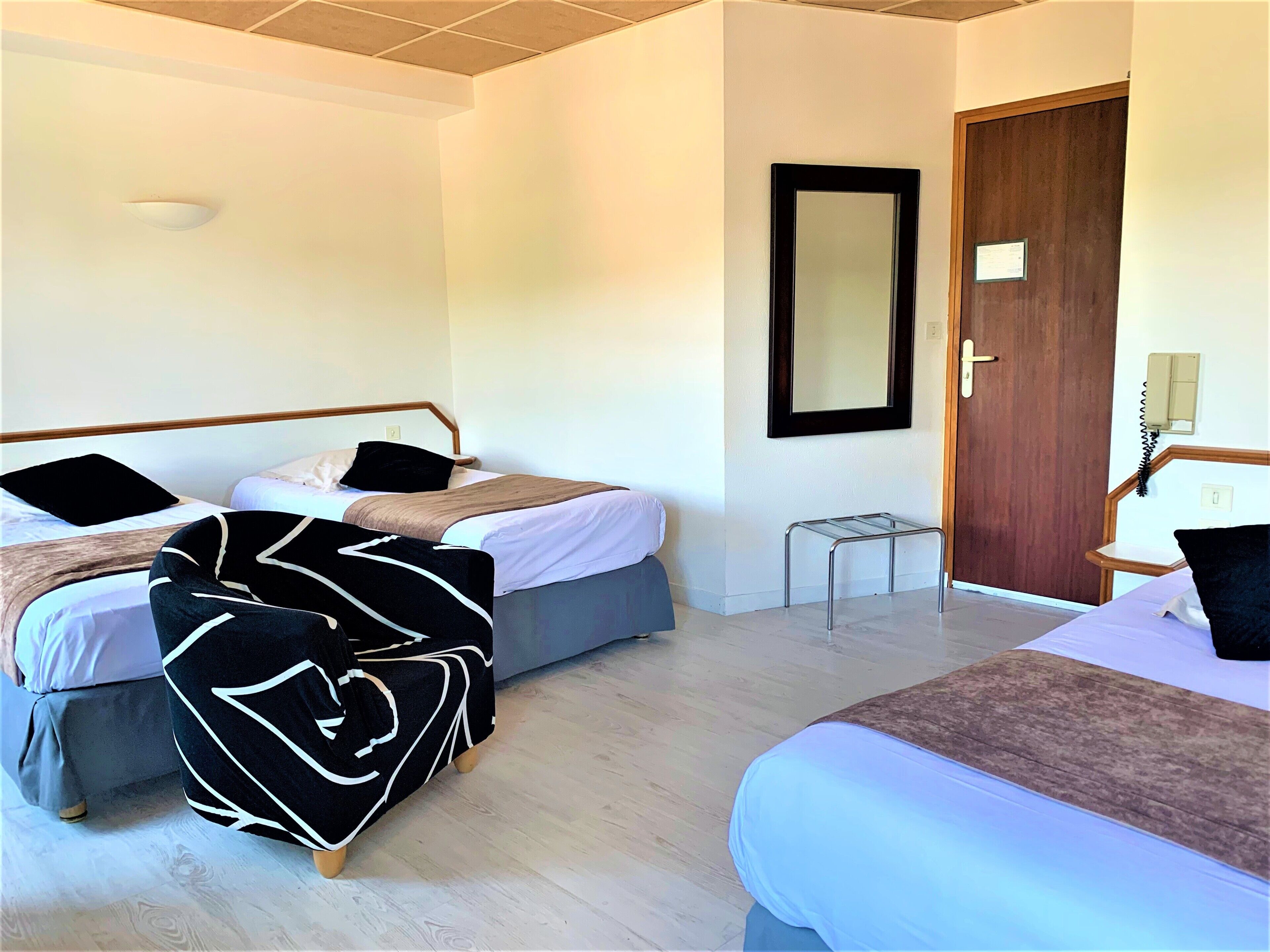A hotel room with two beds, a wooden door, a mirror, and a small table.