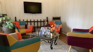Een woonkamer met kleurrijke fauteuils, een glazen salontafel en een flatscreen televisie aan de muur.
