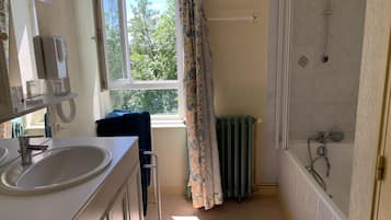 A bathroom with a sink, mirror, window, shower, and radiator.