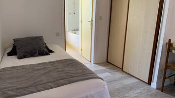Una camera da letto con un letto, un comodino, un armadio e un bagno visibile attraverso una porta aperta.