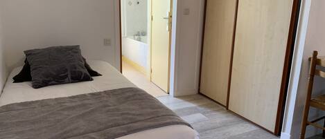 A bedroom with a bed, a bedside table, a wardrobe, and a bathroom visible through an open door.