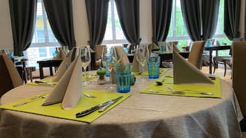 A dining area with tables set for a meal, featuring green placemats, silverware, and blue glassware.