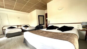 Een hotelkamer met een groot bed, twee kleinere bedden, een houten hoofdbord, een nachtkastje met een lamp en een spiegel aan de muur.
