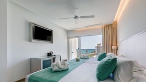 Habitación de hotel con cama, escritorio, televisor y balcón con vista al océano.