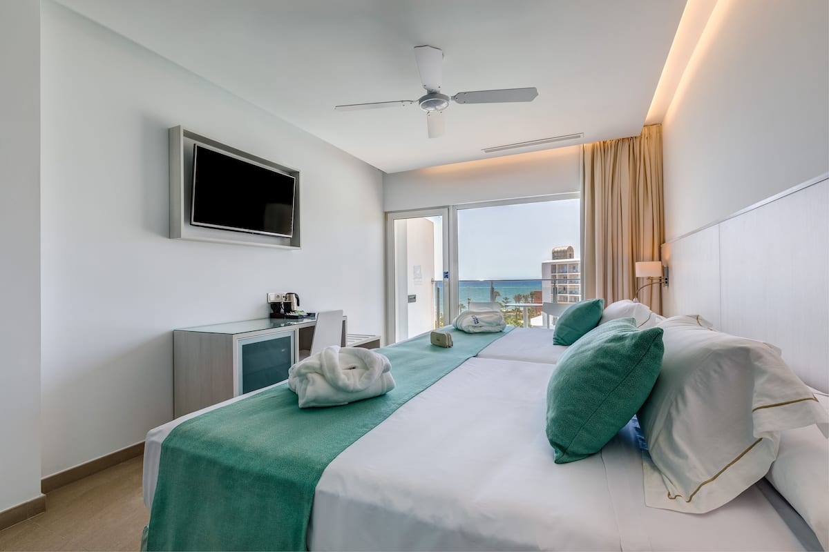 Une chambre d’hôtel avec un lit, un bureau, une télévision et un balcon donnant sur l’océan.