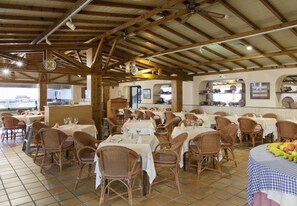 Ein Restaurant mit Holzbalken, Korbstühlen und gedeckten Tischen.