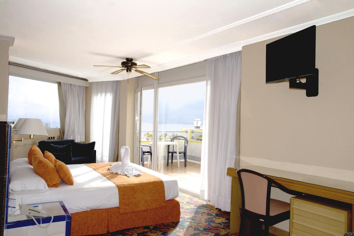 Une chambre d’hôtel comprenant un lit, un bureau, une chaise, une télévision et un balcon avec une table et des chaises.