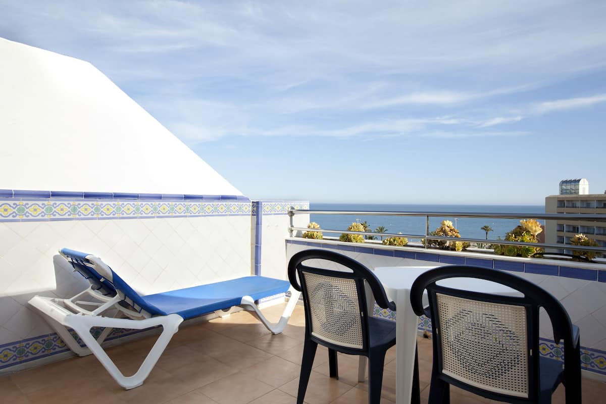 Un balcon avec un transat, deux chaises et une vue sur la mer.
