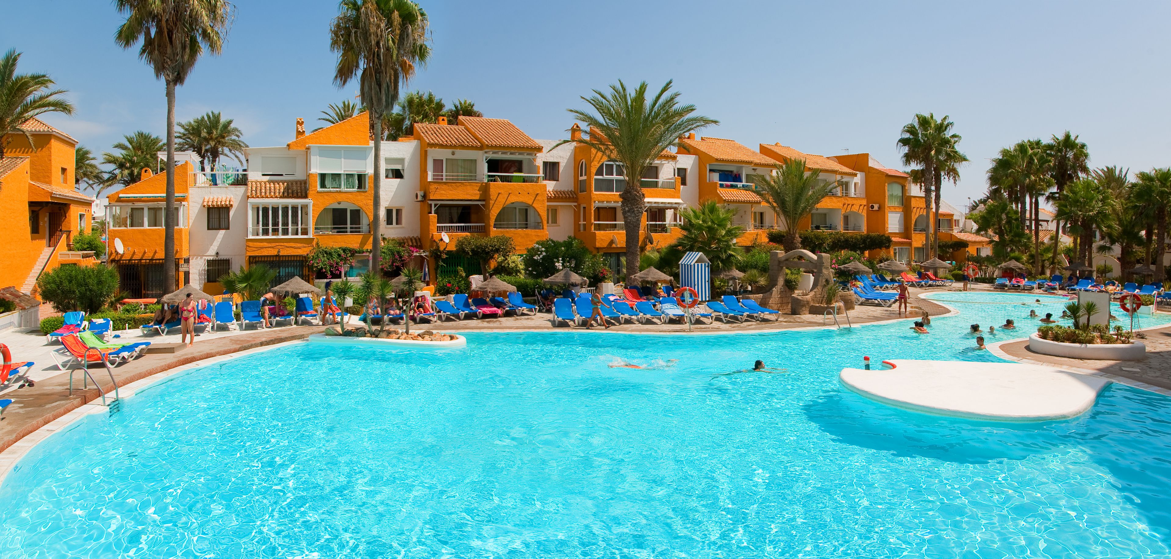 A resort with a large swimming pool, palm trees, and colorful lounge chairs.