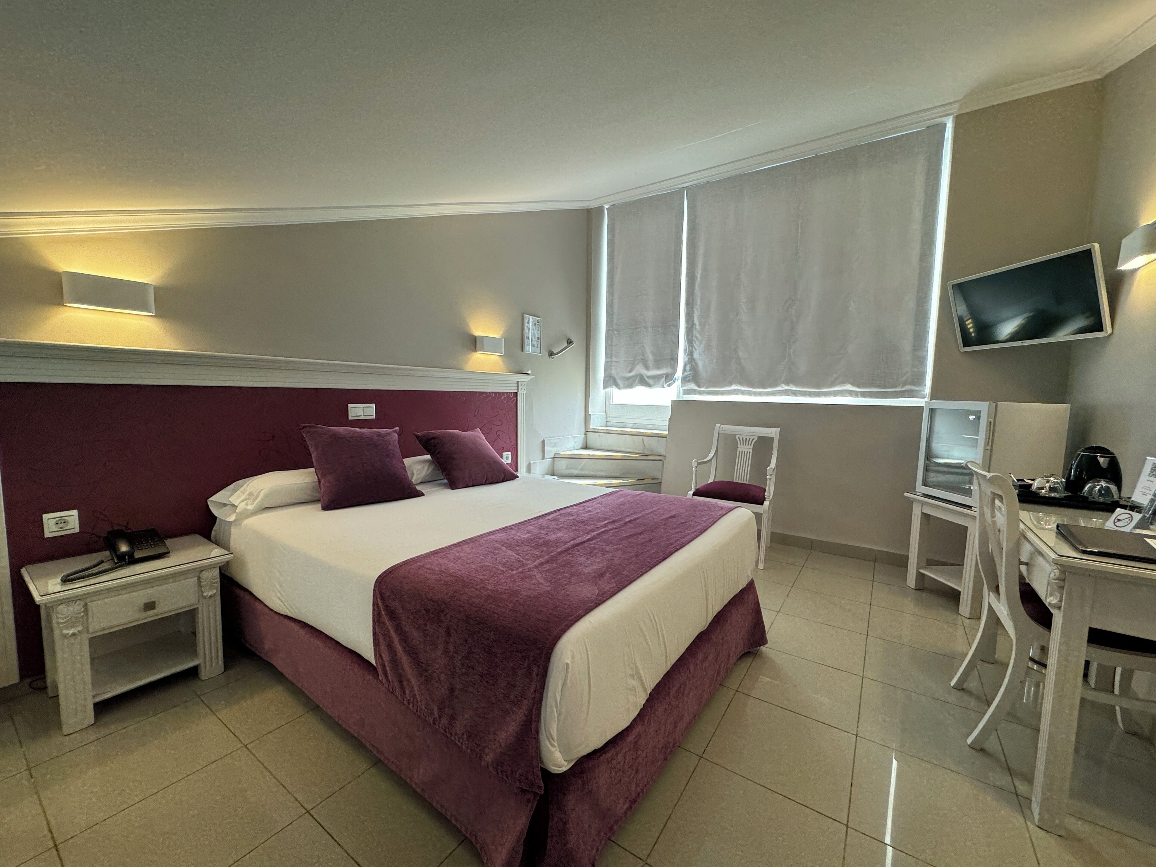 A hotel room with a bed, a desk, a chair, a television, and a window with curtains.